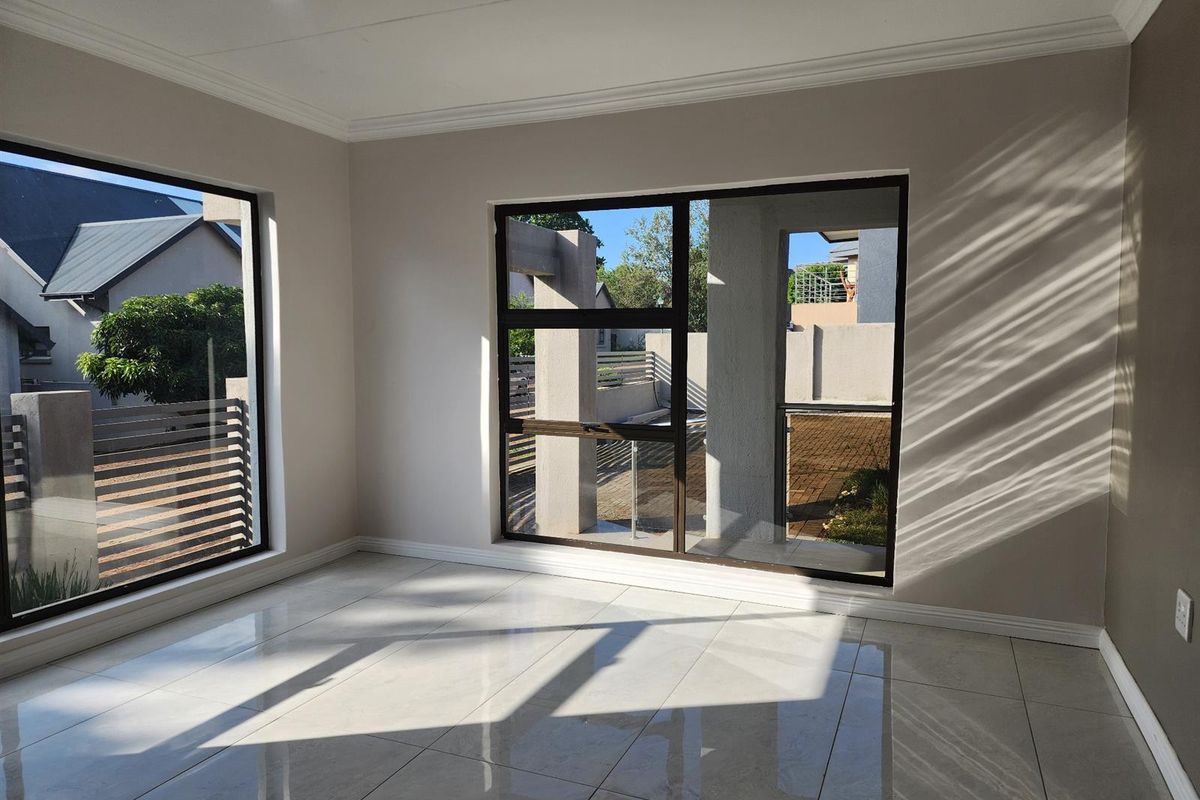 A bright, empty living area featuring large windows, modern tiled flooring, and neutral wall finishes, offering a clean and versatile space.