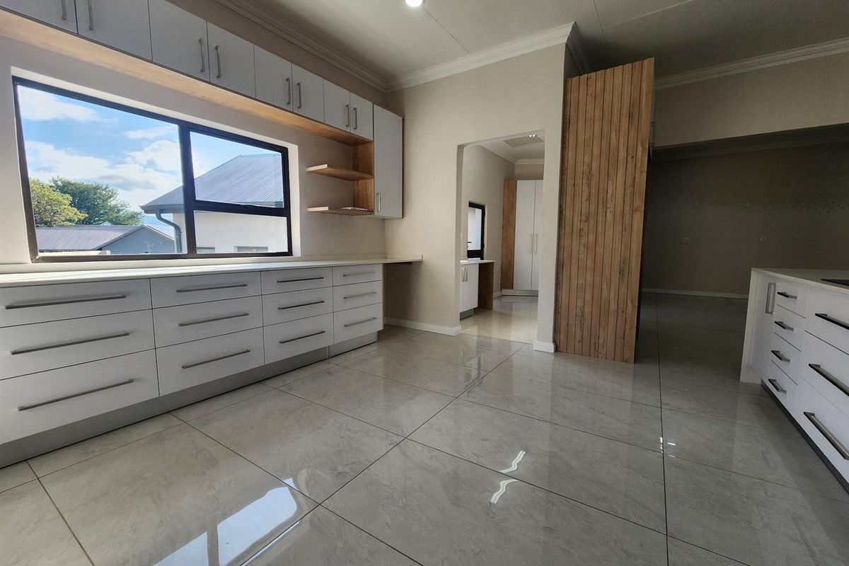 Modern kitchen featuring sleek white cabinetry, polished tile flooring, and a large window providing ample natural light, with an adjacent scullery area.