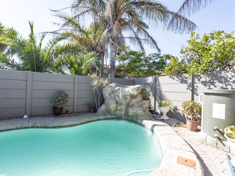 A private outdoor pool area featuring a decorative rock water feature, paved surround, and secure precast concrete boundary walling.