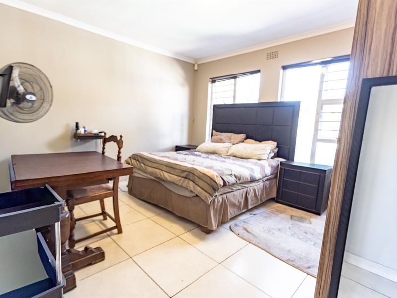 A bedroom featuring tiled flooring, louvered windows, and neutral wall finishes.