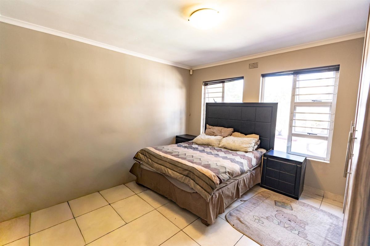 A functional bedroom featuring tiled flooring, aluminium window frames with security bars, and a neutral wall finish.