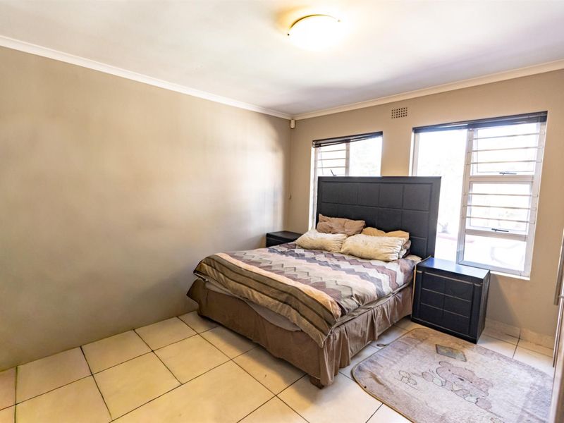 A functional bedroom featuring tiled flooring, aluminium window frames with security bars, and a neutral wall finish.