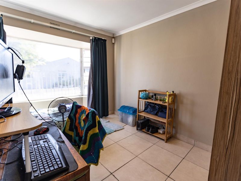 A bedroom featuring tiled flooring and a large bay window, currently utilized as a home office space.
