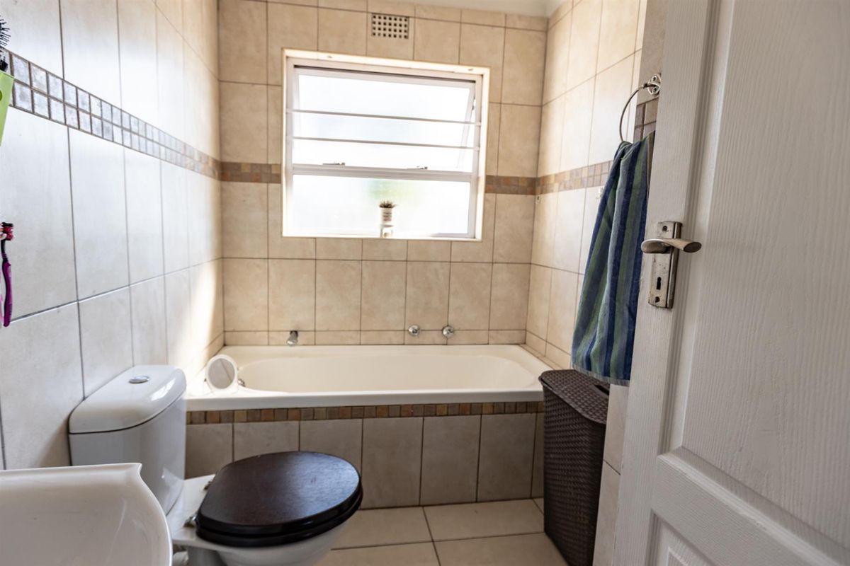 A functional bathroom featuring a built-in bathtub, ceramic wall and floor tiling, and a standard toilet with a window for natural light.