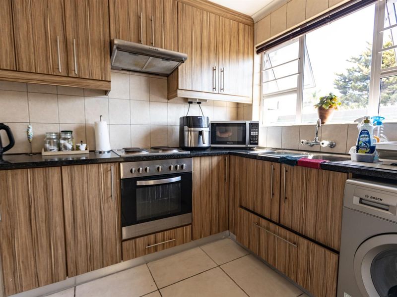 A functional kitchen featuring wood-grain laminate cabinetry, granite countertops, built-in oven, electric hob, and integrated space for a washing machine.