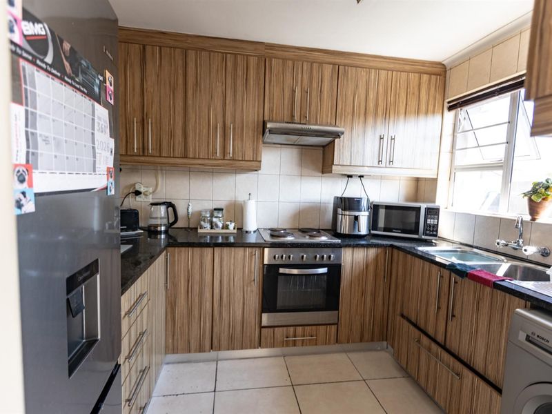 A functional kitchen featuring wood-look laminate cabinetry, granite countertops, a built-in oven with hob, and tiled flooring.