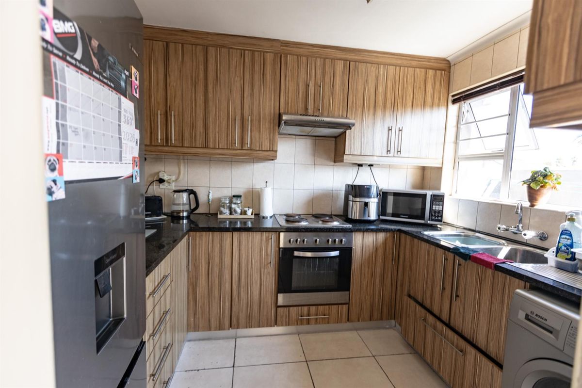 A functional kitchen featuring wood-look laminate cabinetry, granite countertops, a built-in oven with hob, and tiled flooring.