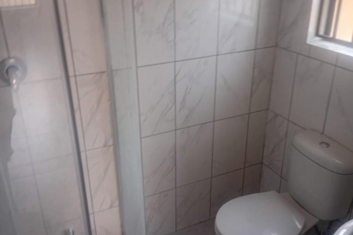 A functional bathroom featuring a glass-enclosed shower, tiled walls, and a standard toilet suite with natural light from a side window.