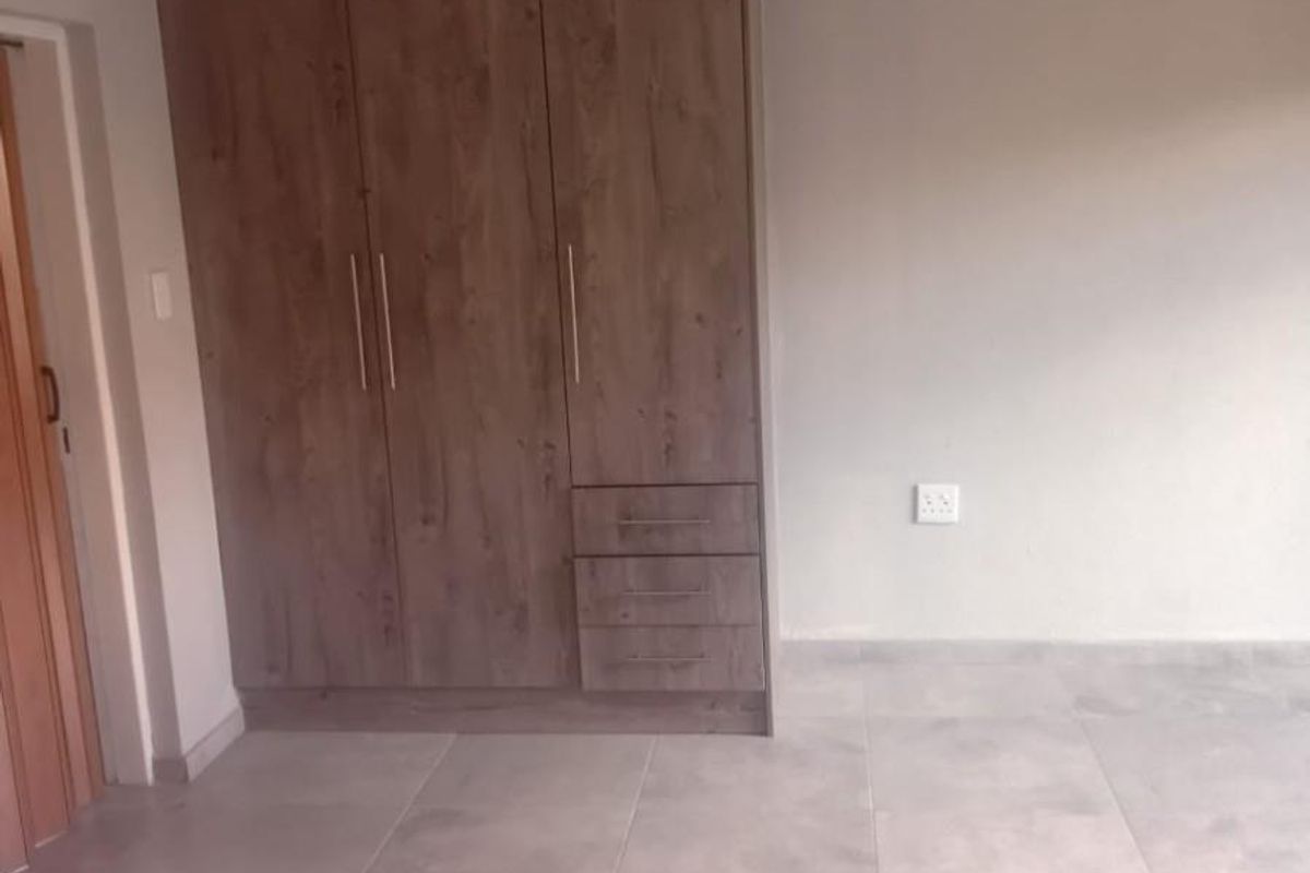 A bright bedroom featuring neutral tiled flooring and a modern, built-in wooden wardrobe with integrated drawers.