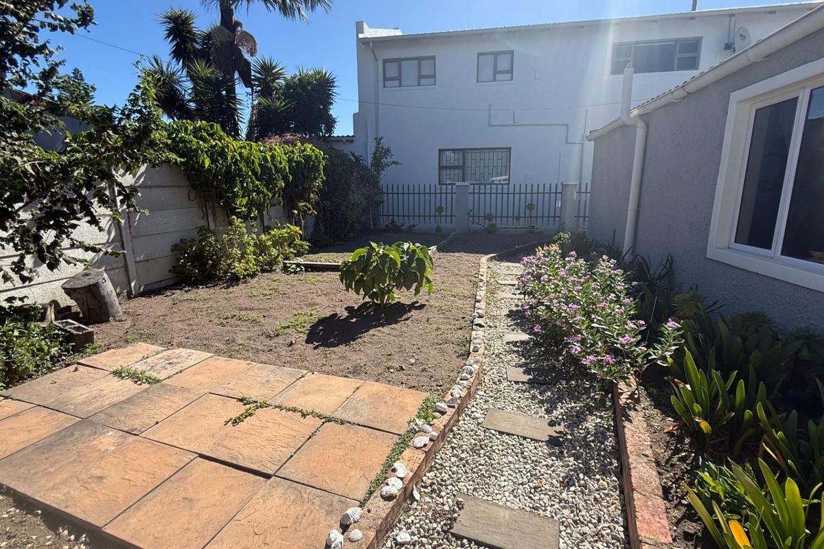 A rear garden area featuring a paved patio section, gravel pathway, and established garden beds alongside the property exterior.