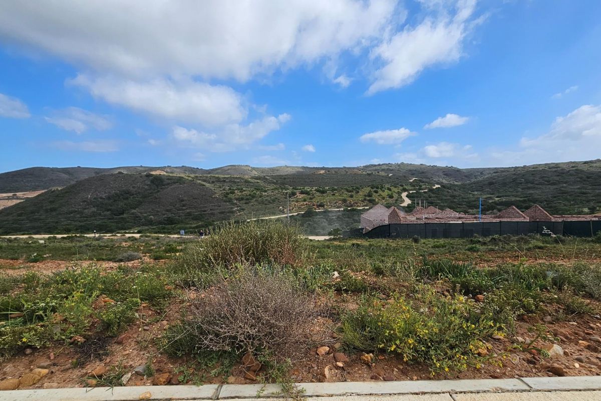 A wide-angle view of the vacant residential land, showcasing the natural landscape, surrounding hills, and nearby development.