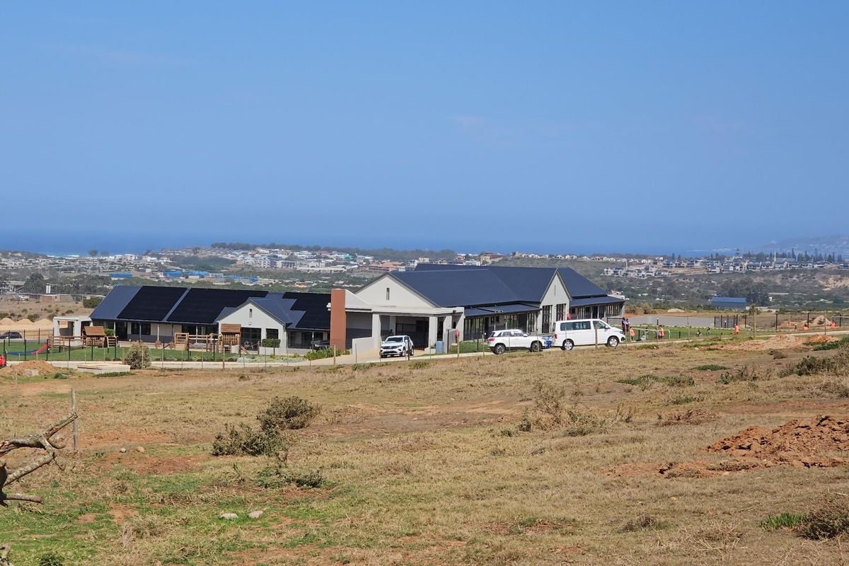 An elevated view of a modern residential building complex situated on a large plot of land with coastal views in the distance.