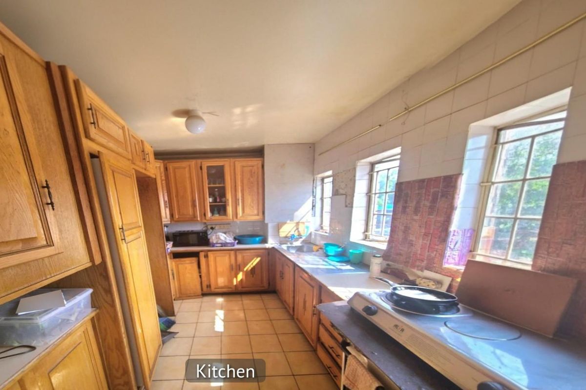A dated kitchen featuring traditional wooden cabinetry, tiled flooring, and built-in counter space with natural light from multiple windows.