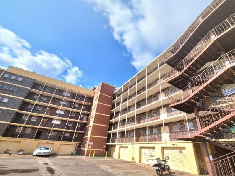Exterior view of a multi-story residential apartment building featuring brick facade, external metal staircases, and ground-level garage access.
