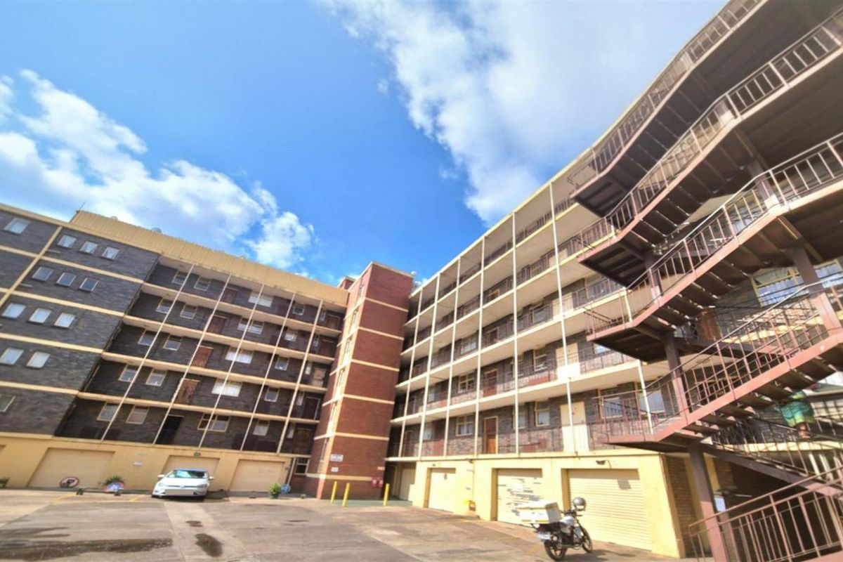 Exterior view of a multi-story residential apartment building featuring brick facade, external metal staircases, and ground-level garage access.