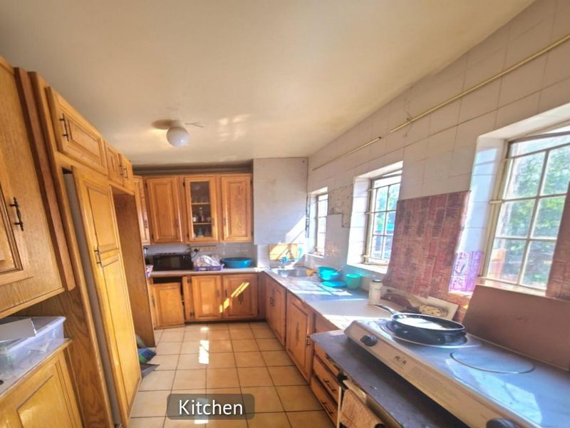 A dated kitchen featuring traditional wooden cabinetry, tiled flooring, and built-in counter space with natural light from multiple windows.