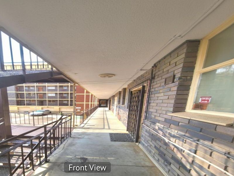 An exterior walkway providing access to residential units, featuring brick facade walls, concrete flooring, and an external metal staircase.