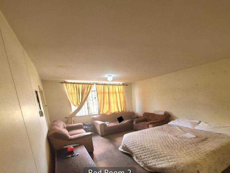 A spacious bedroom featuring neutral walls, carpeted flooring, and a window with curtain fixtures, offering a functional layout for a primary or guest suite.
