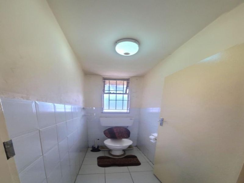 A compact, functional bathroom featuring a standard toilet, tiled walls, and a window for natural light.