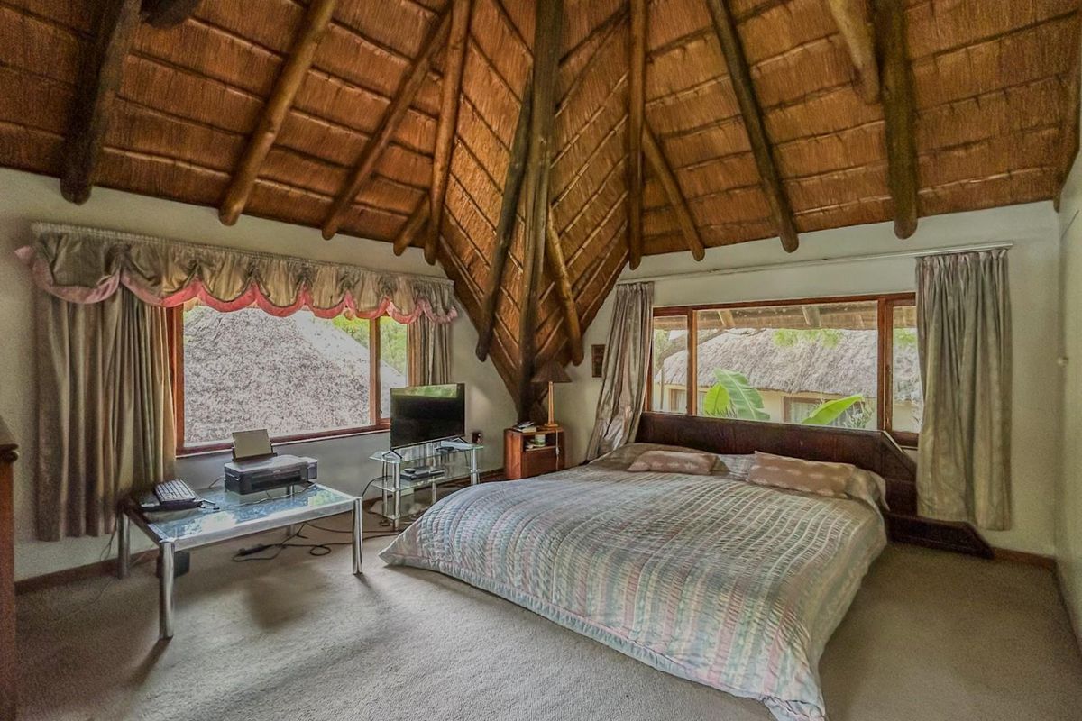 Spacious bedroom featuring a high vaulted thatched ceiling with exposed timber rafters, large windows, and built-in storage.