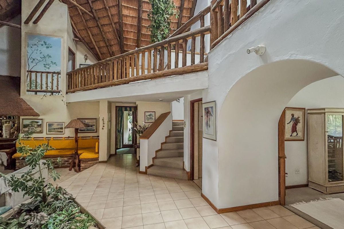 Spacious living area featuring a high thatched ceiling, mezzanine level with timber railing, tiled floors, and unique architectural arched transitions.