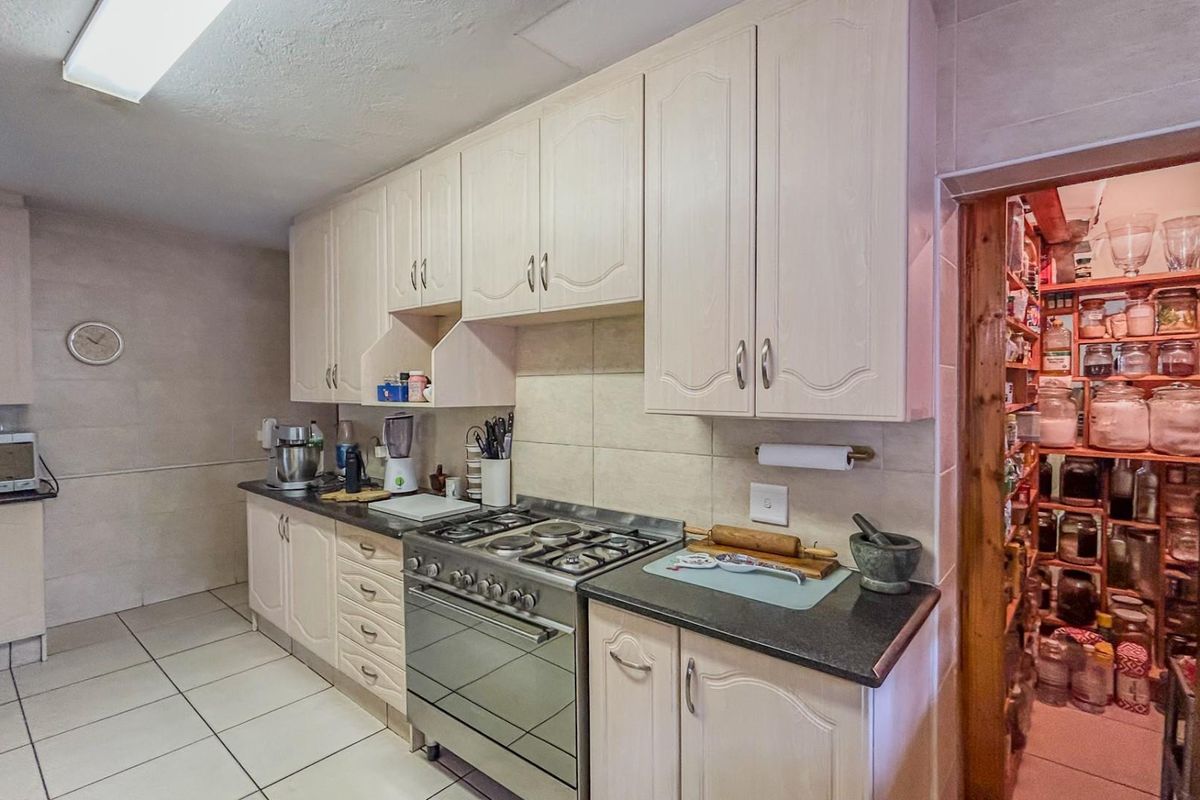 A functional kitchen featuring light-toned cabinetry, a gas stove with oven, tiled flooring, and an adjacent walk-in pantry for additional storage.