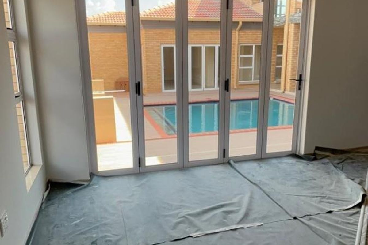 Bright living area featuring large folding glass doors that open directly onto a private swimming pool and outdoor patio space.