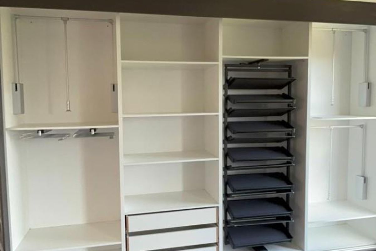 A spacious, modern built-in wardrobe featuring integrated shelving, hanging rails, and pull-out storage drawers, providing ample organized storage space.