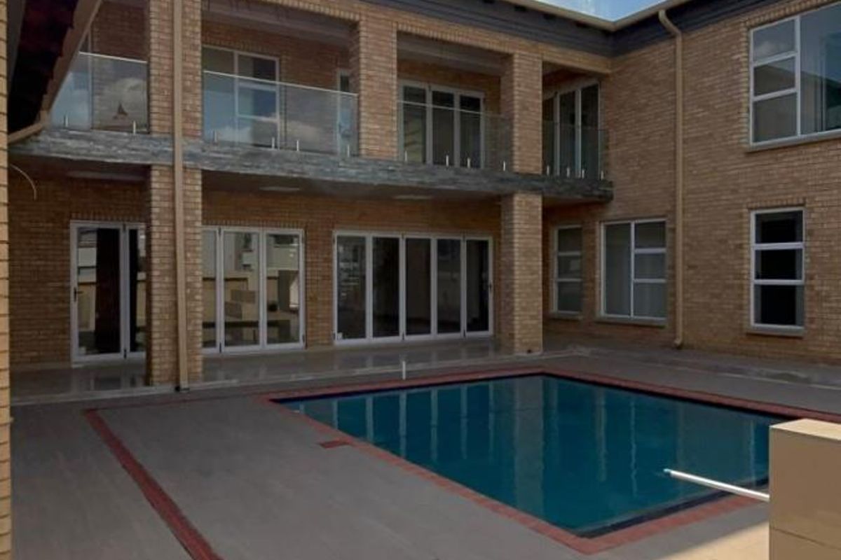A spacious rear courtyard featuring a swimming pool, tiled patio area, and a two-story brick facade with glass balcony railings.