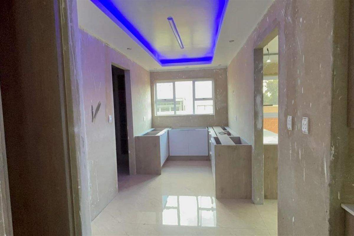 An unfinished kitchen space featuring tiled flooring, recessed ceiling lighting with blue LED accents, and partially installed cabinetry units.