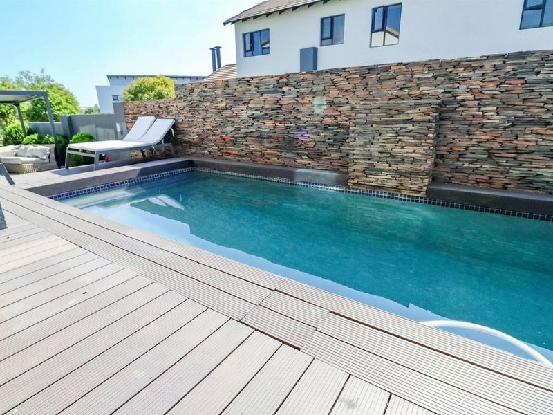 A well-maintained swimming pool area featuring a decorative stone feature wall and modern composite decking surround.
