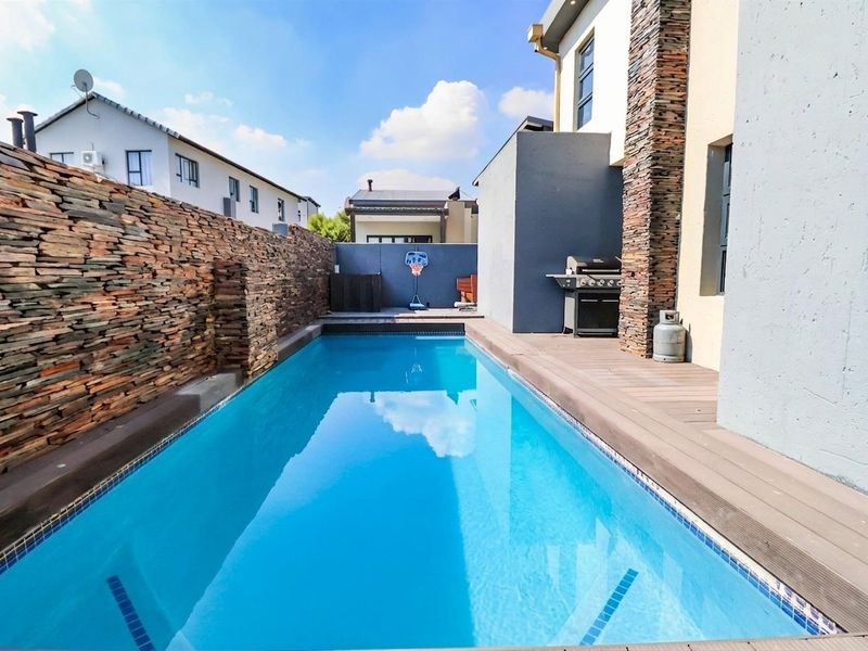 A well-maintained swimming pool area featuring modern timber decking and decorative stone cladding on the boundary wall.