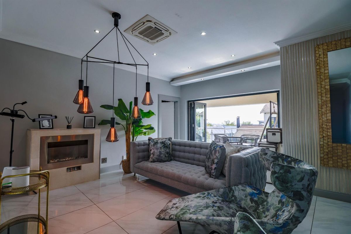 Modern living room featuring a built-in fireplace, recessed ceiling lighting, ducted air conditioning, and large folding doors opening to an outdoor patio area.