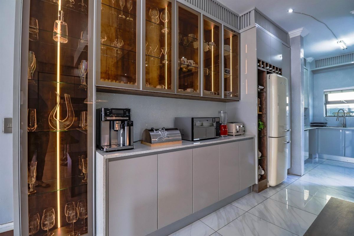 Modern kitchen featuring sleek cabinetry, integrated glass-front display shelving with accent lighting, stone countertops, and high-gloss floor tiles.