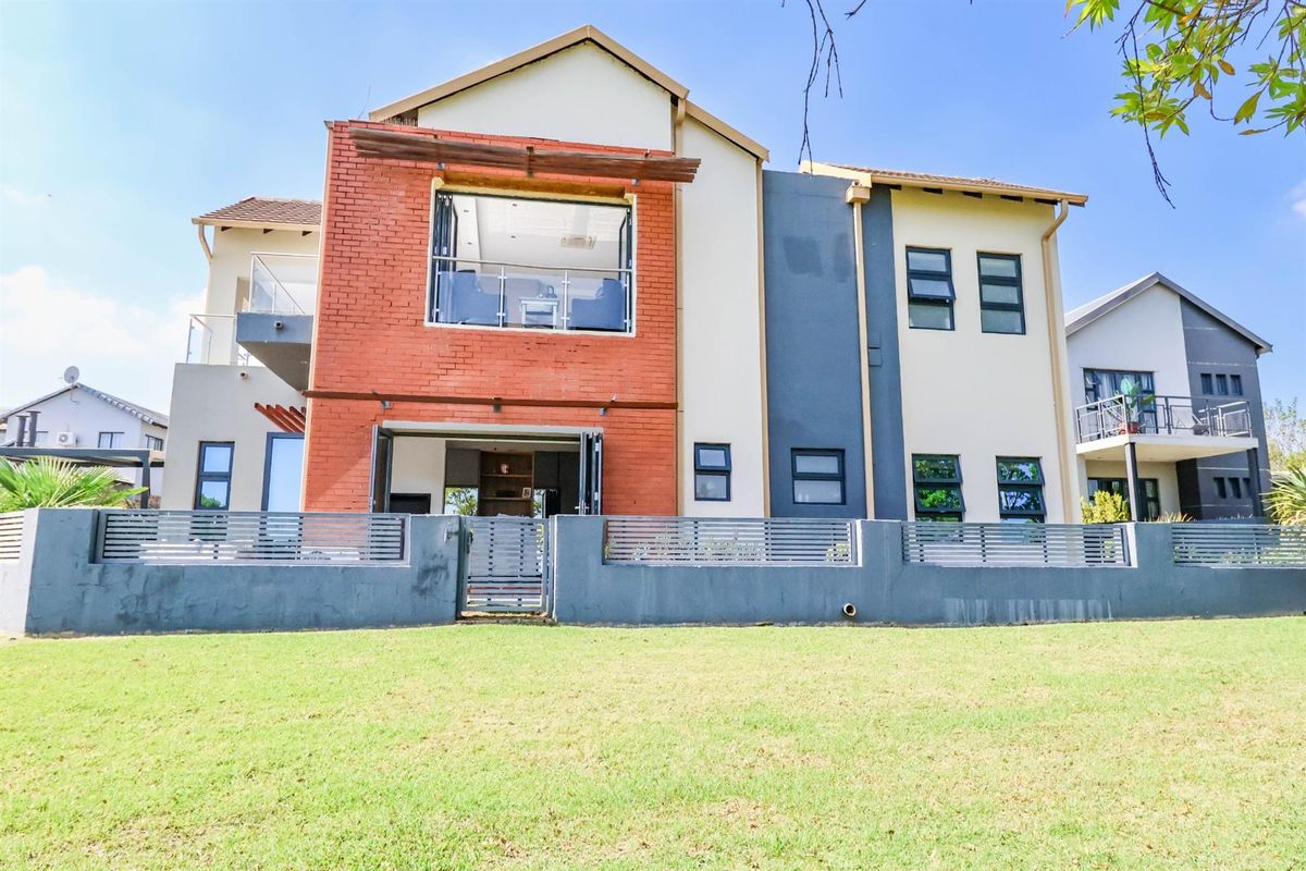 A modern double-story residential property featuring a combination of brick and rendered facade, large windows, and a private fenced garden area.