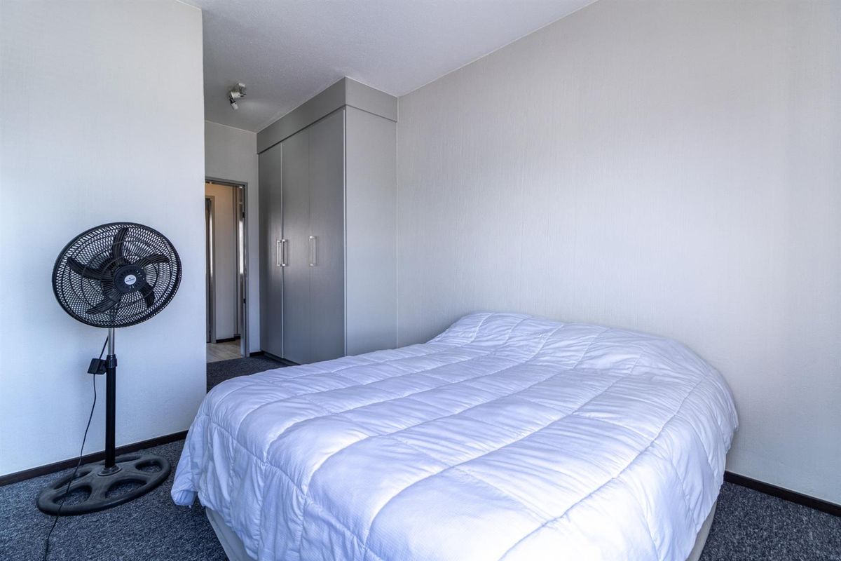A functional bedroom featuring neutral walls, carpeted flooring, and a built-in wardrobe for storage.