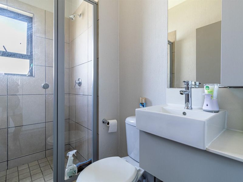 A functional bathroom featuring a glass-enclosed shower, modern vanity basin with mixer tap, toilet, and a wall-mounted mirror.