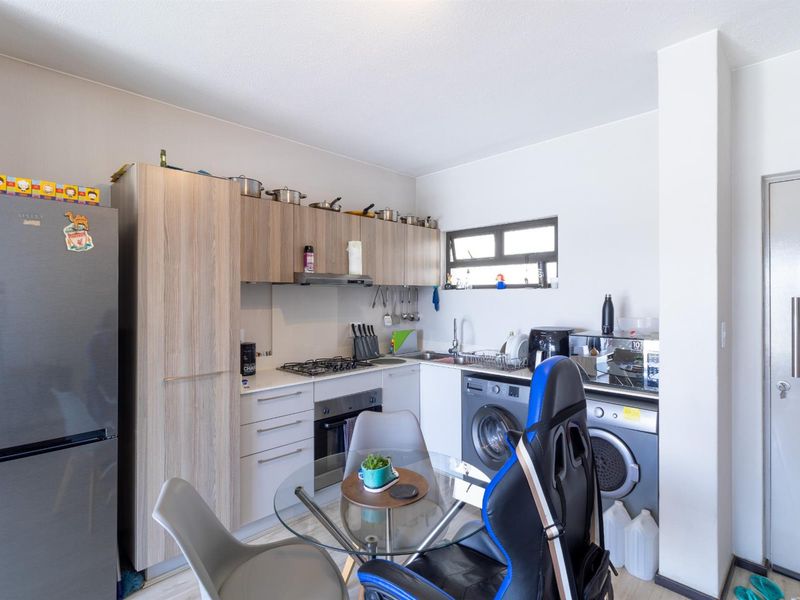 Compact kitchen featuring light wood-finish cabinetry, built-in gas hob, oven, extractor fan, and integrated laundry plumbing connections.
