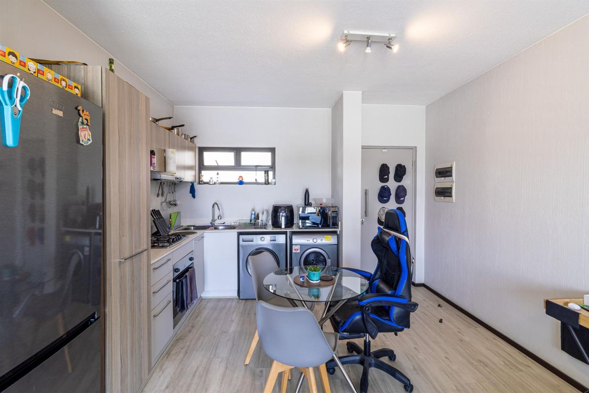 Compact kitchen featuring modern wood-look cabinetry, integrated laundry appliances, built-in oven and hob, and durable laminate flooring.
