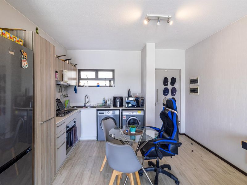 Compact kitchen featuring modern wood-look cabinetry, integrated laundry appliances, built-in oven and hob, and durable laminate flooring.