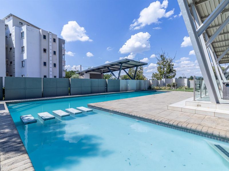 A well-maintained outdoor swimming pool area featuring a paved deck, integrated stepping stones, and a modern metal-roofed structure.