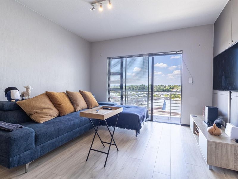 A bright living room featuring light laminate flooring and a sliding glass door that opens onto a balcony with an elevated view.