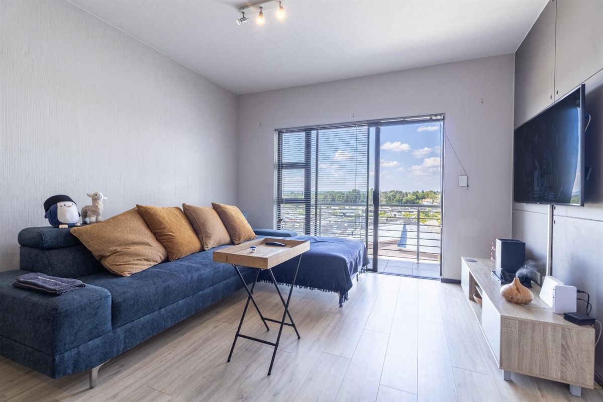 A bright living room featuring light laminate flooring and a sliding glass door that opens onto a balcony with an elevated view.