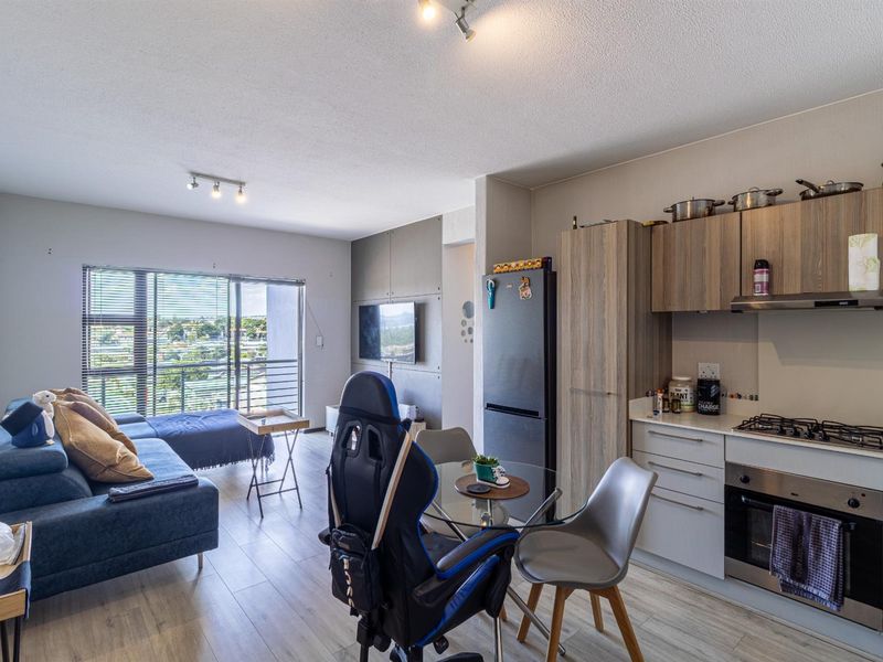 Open-plan living area featuring a modern kitchen with built-in appliances, laminate flooring, and a sliding glass door leading to a balcony with views.