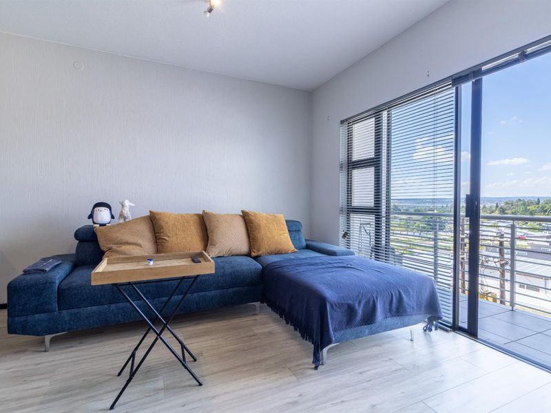 A bright living room featuring light laminate flooring and a large sliding glass door that opens onto a balcony with expansive views.