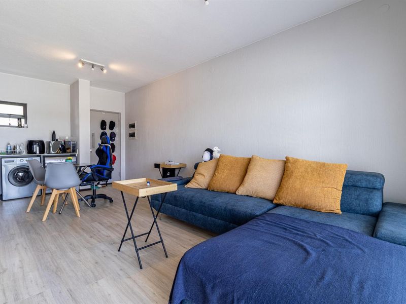 Open-plan living area featuring light laminate flooring, neutral walls, and a compact kitchen corner with built-in cabinetry and integrated laundry facilities.