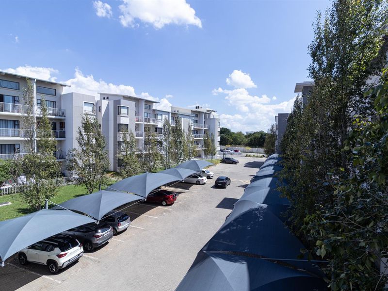 An elevated view of the apartment complex parking area featuring covered shade cloth carports and well-maintained surrounding landscaping.