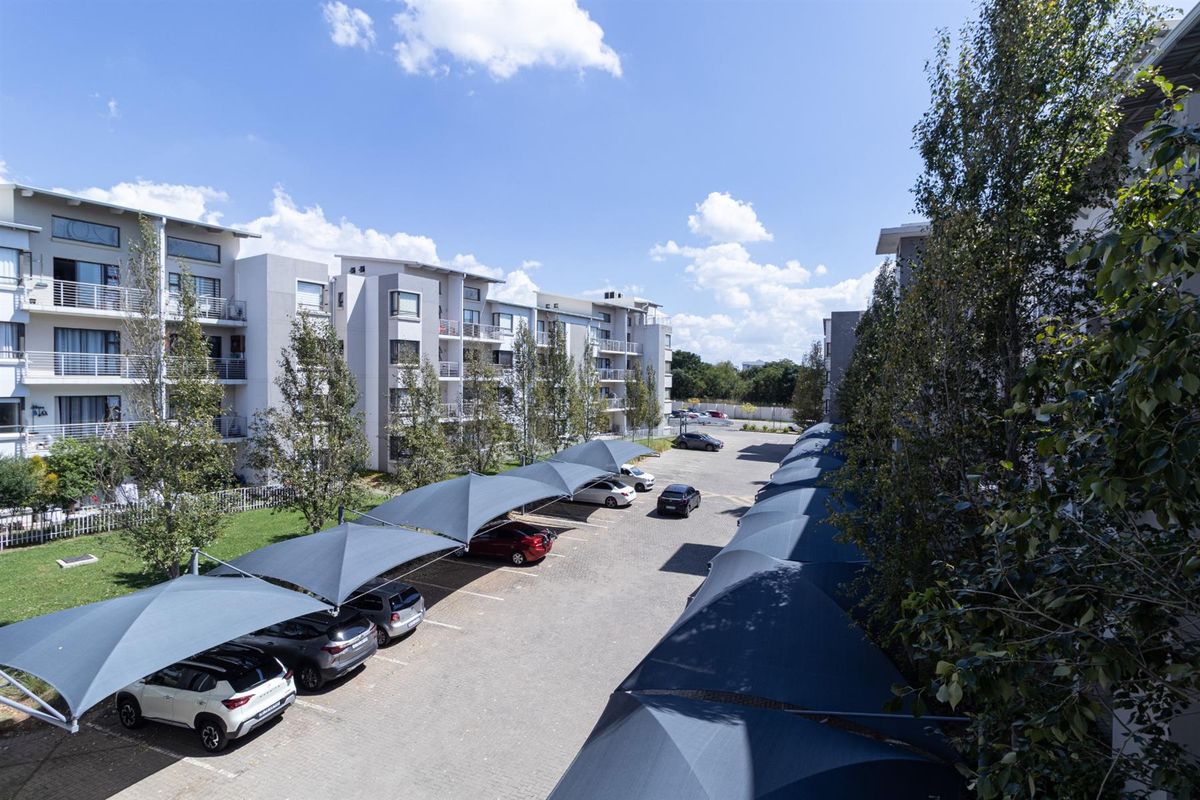 An elevated view of the apartment complex parking area featuring covered shade cloth carports and well-maintained surrounding landscaping.