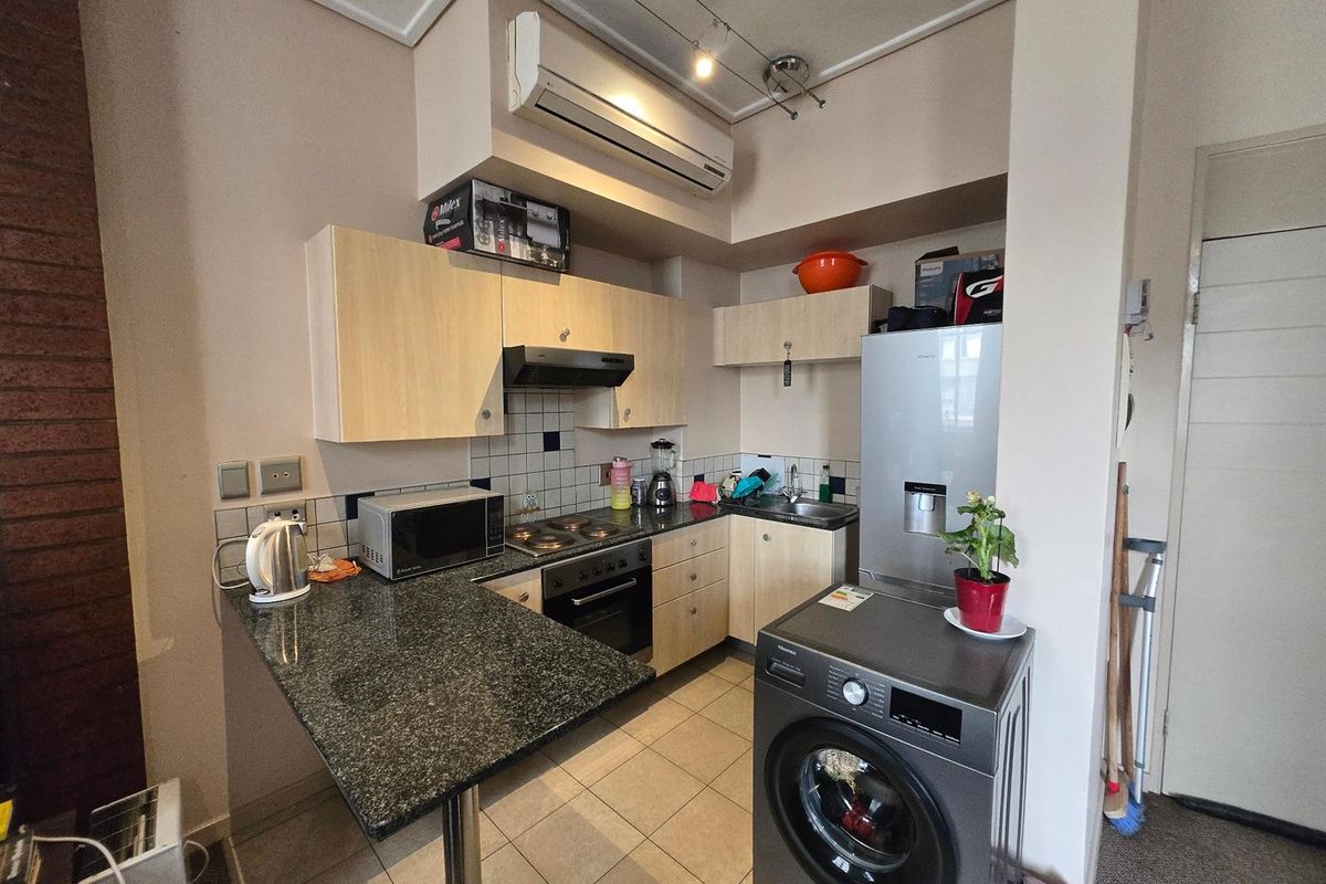 Compact kitchen featuring granite countertops, built-in oven with hob, extractor fan, and tiled backsplash, with an integrated air conditioning unit.