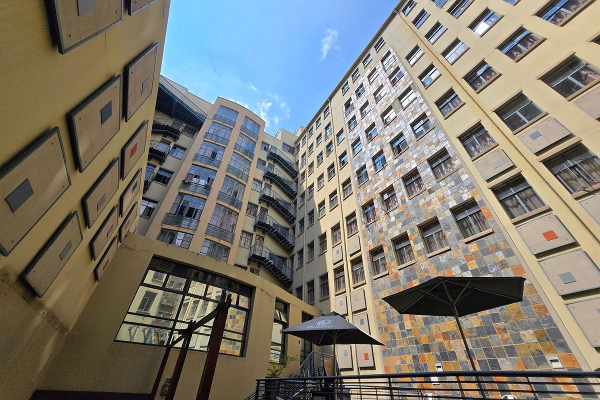 A low-angle view of the apartment building's rear courtyard, featuring stone-clad walls, metal fire escapes, and multi-story window arrangements.